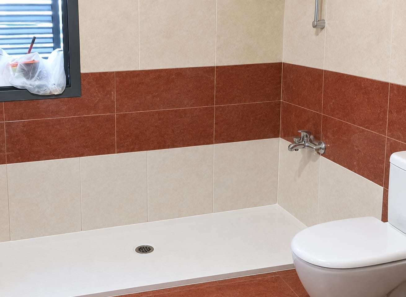 Plato de ducha blanco extraplano instalado en lugar de una bañera, con azulejo beige y granate